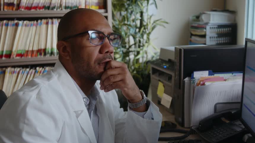 Doctor thinks while sitting in front of computer near files