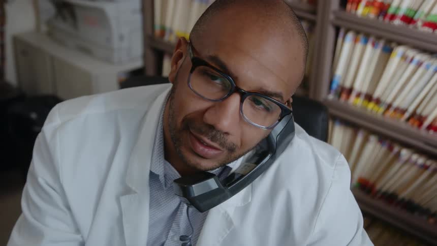 Man sits in room near shelves full of medical files and talks on phone