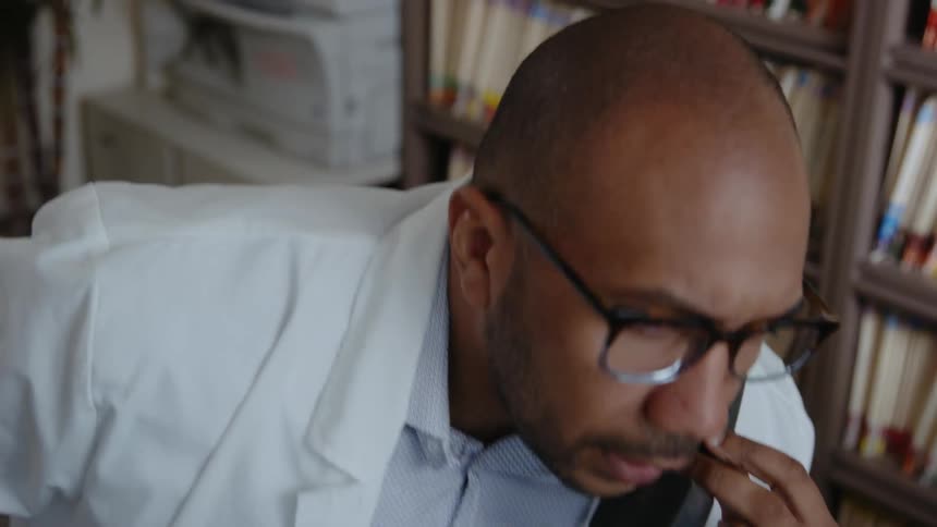Doctor sitting near shelves of color coded files talks on phone