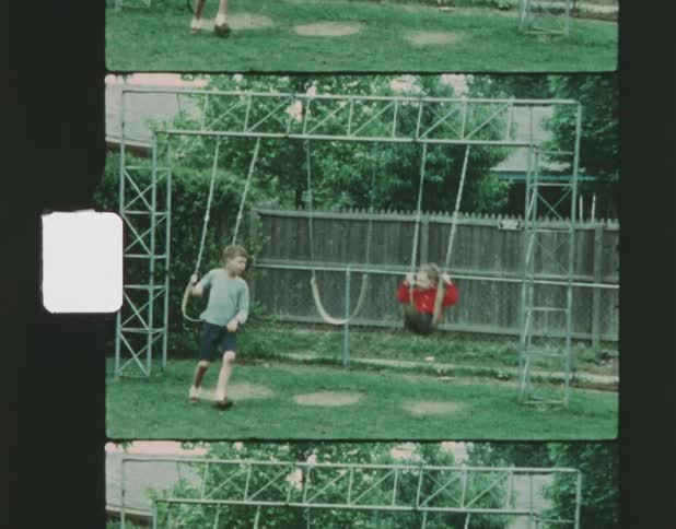 Two little boys are riding swings on a backyard swing set as one boy gets off the swing he is riding and moves to the next swing