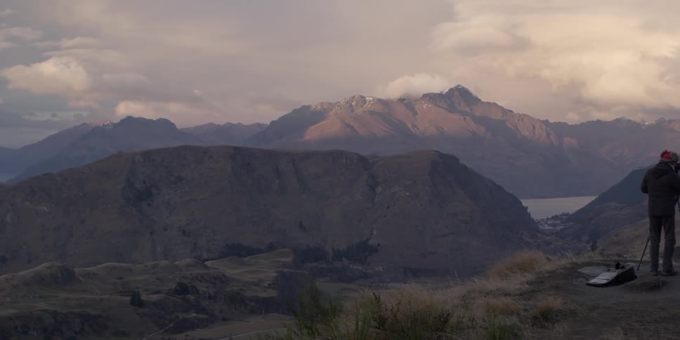 A couple take pictures on a hill near a mountain
