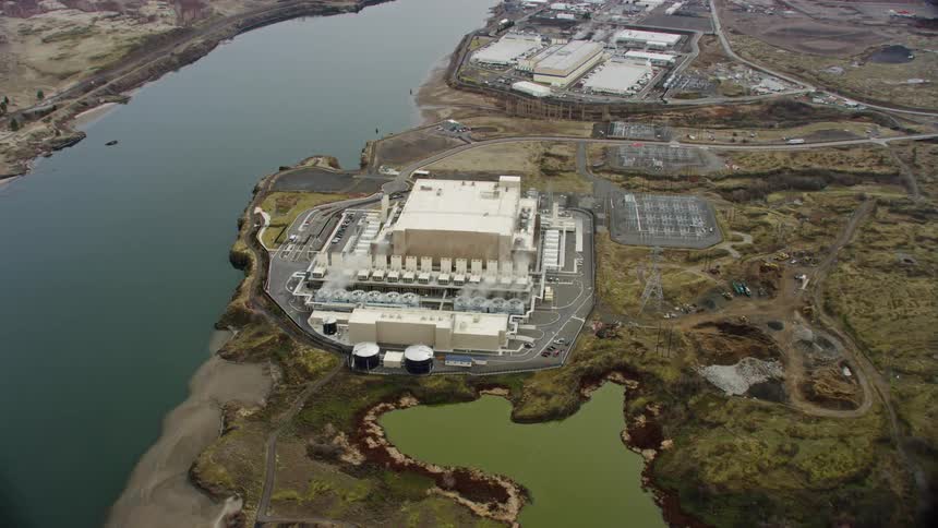 An aerial overhead view of a factory in a grassy developed area next to a river