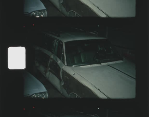 Damaged station wagon sits parked with other cars at night