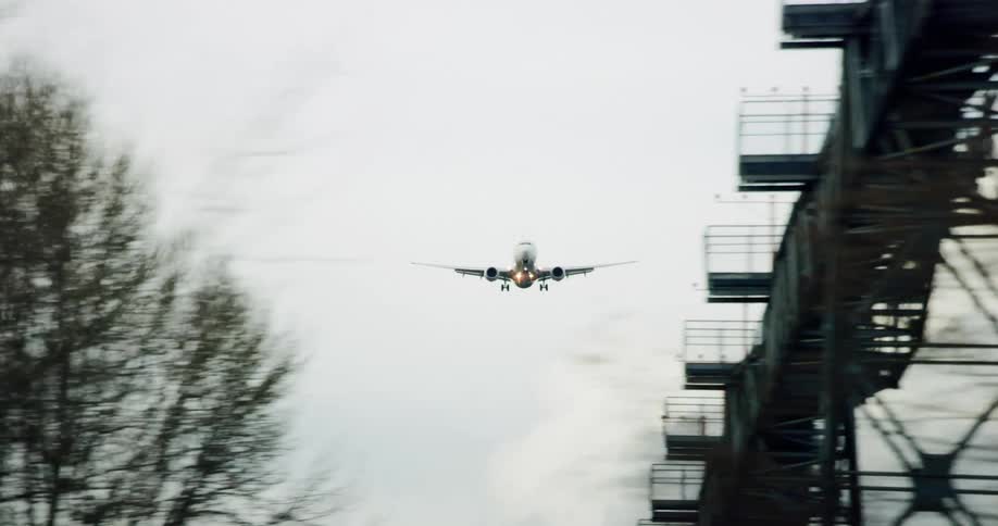 An airplane descending in the air over vegetation and towers