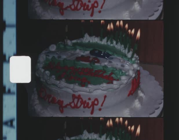 A cake with candles on it covered in white frosting writing and toy cars