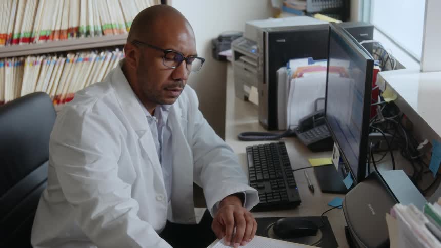 Doctor sitting in office reviewing patients chart look on face says prognosis isnt good
