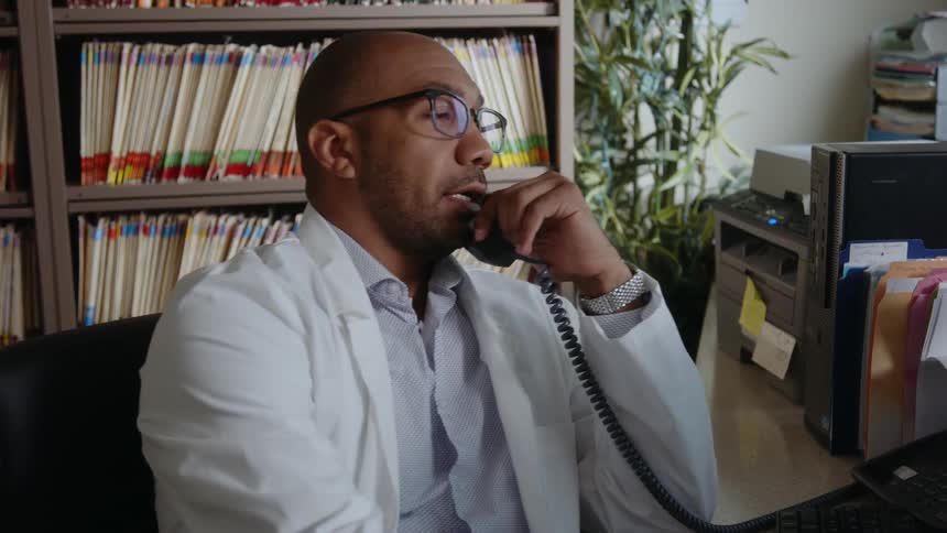 Busy man in his office engrossed in taking calls surrounded by a vast collection of books neatly arranged on his office shelf reflecting his knowledge and dedication to his work