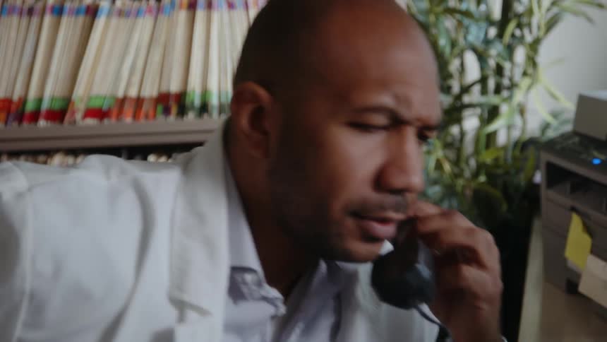 Doctor talks on phone while sitting in office near shelves of files