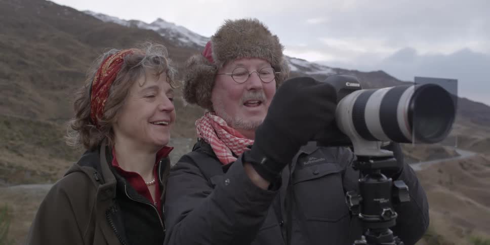 A man and woman look at a camera