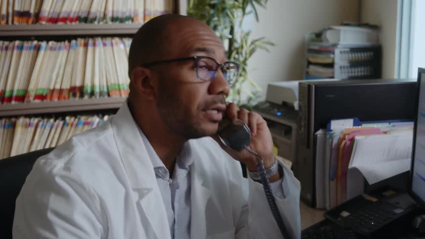 A male physician shakes his head while talking on the phone