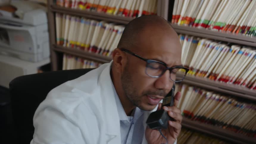 A doctor talks on the phone in an office and reacts to what hes told