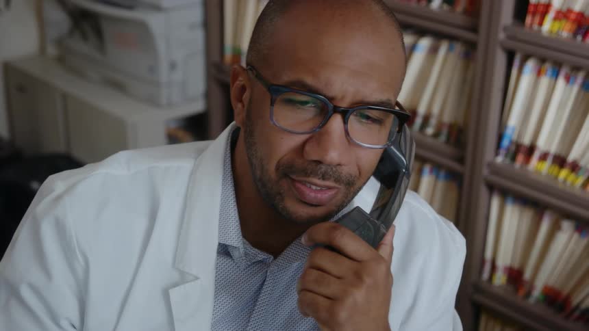 A doctor in an office talks on the phone and smiles