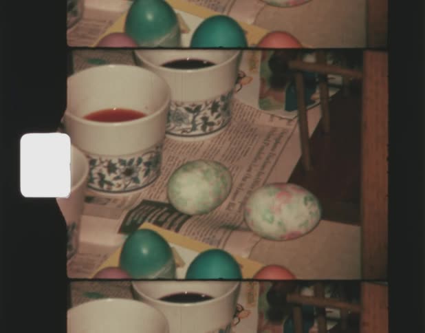 Three cups contain dye used to color some nearby eggs on a table