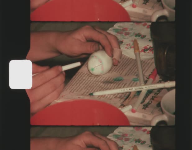 A girl is holding an egg as she draws on the shell with colored markers