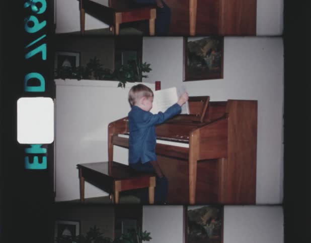 A young boy putting a song book on a piano whle sittin gon the piano bench