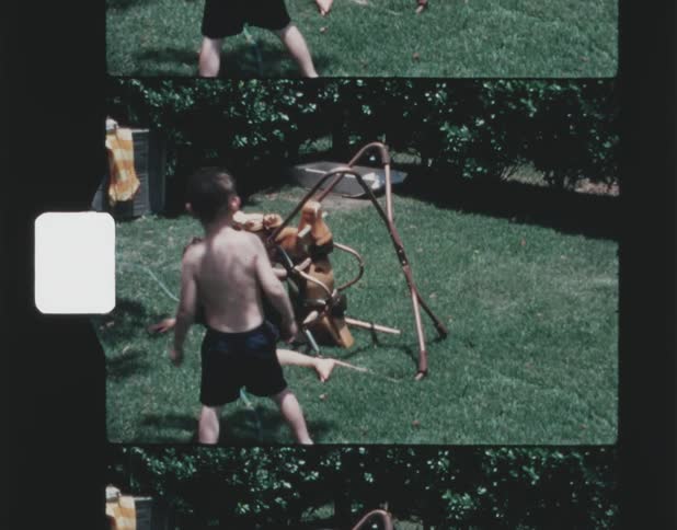Vintage footage of two little boys brothers playing with rocking horse and a hose in the back yard in the summer