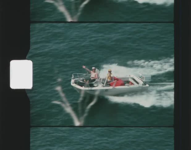 A man waves as he and a woman ride on a fast moving motor boat