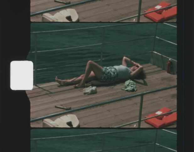 A woman is sunbathing with lying on a wooden dock thats gently swaying on the water