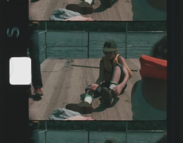 Boy laces his shoes while sitting with his family on boards near water