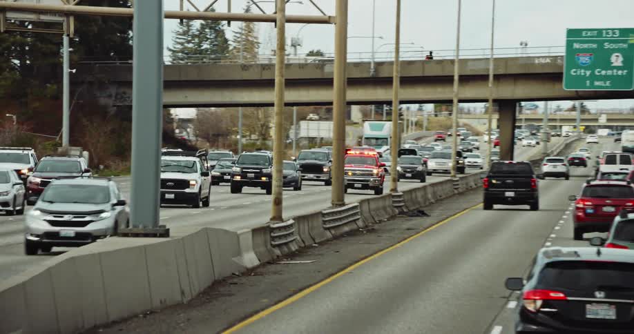 An emergency vehicle races along the freeway with its lights and sirens on as the camera smoothly whip pans to follow it