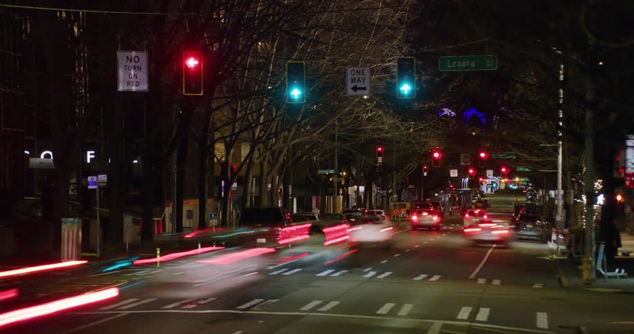 A night time timelapse of a busy downtown street as stop lights change from green to red and traffic flows in all directions