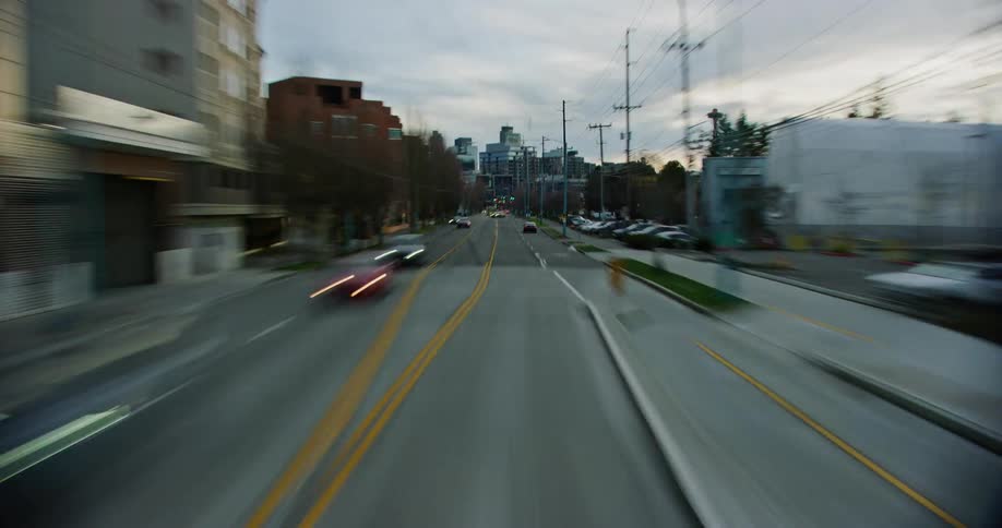A vehicle speeds across a city road passing traffic and buildings