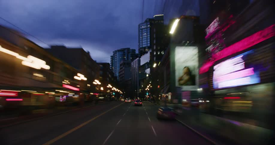 A bustling metropolis illuminated by the night characterized by towering skyscrapers and the exhilarating sight of cars whizzing by at high speeds