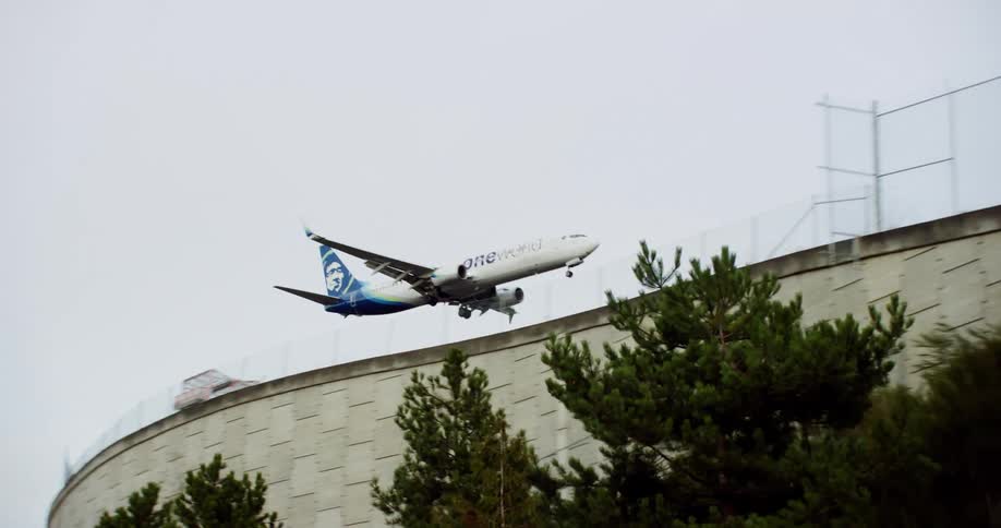 An airplane descending into an airport to land disappearing behind the airport wall