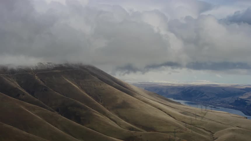 An aerial of clouds hovering over a mountain region casting shadows over it