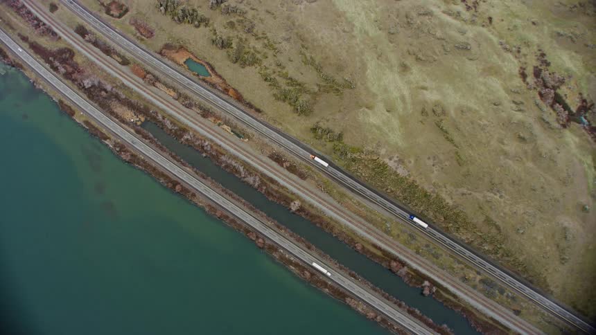 An orbiting aerial view of a highway near a coastal waterway