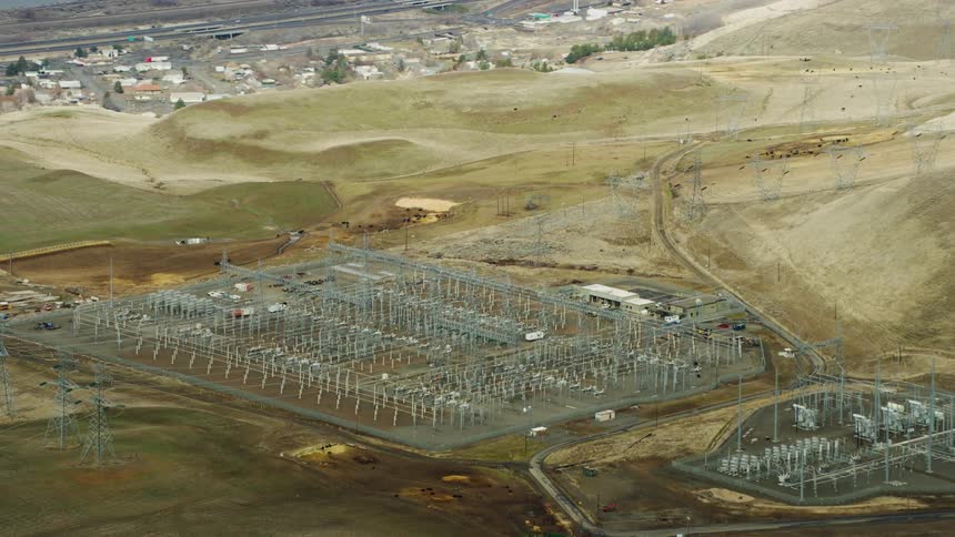 An aerial of a power plant in a valley between hills with a suburb and highway on the other side of the hills
