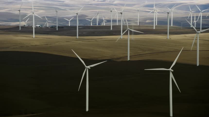 High energy aerial shot of many wind turbines spinning creating renewable energy on a vast wind farm on a moody and high contrast day