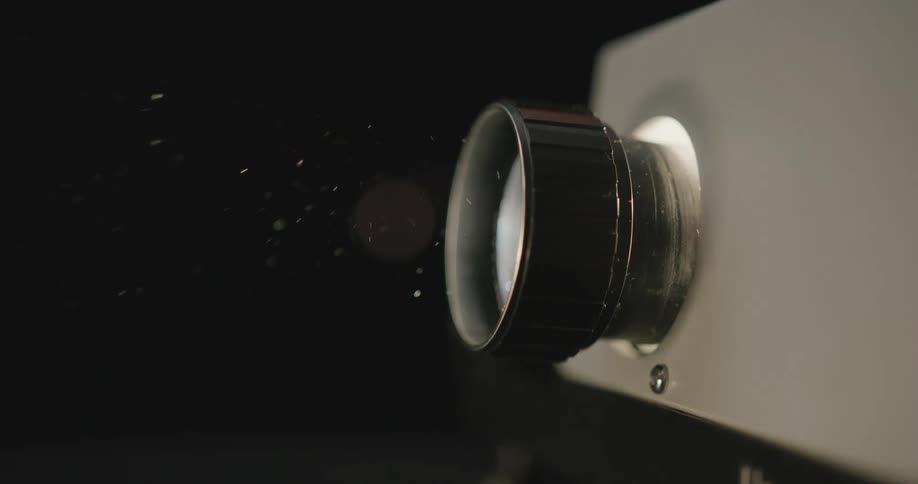 The light of a slide projector flashes in the darkness as dust floats in front of the lens