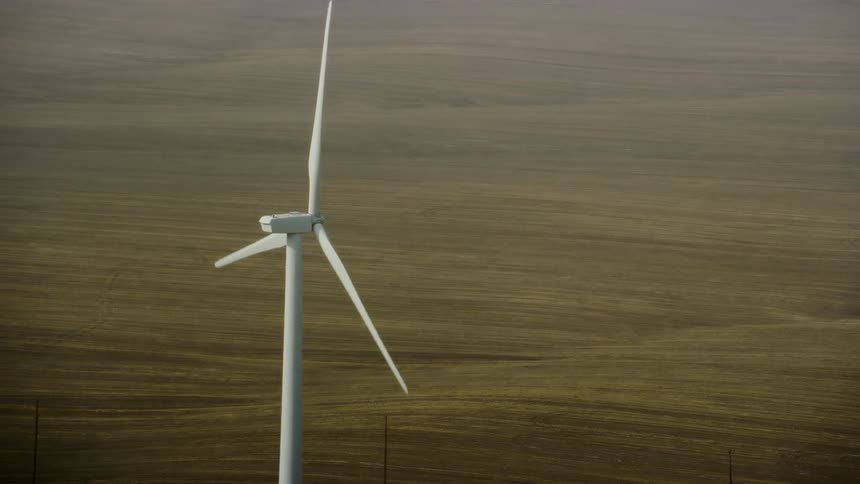 Aerial shot of a lone wind turbine windmill spinning generating renewable clean and green energy in a rural field
