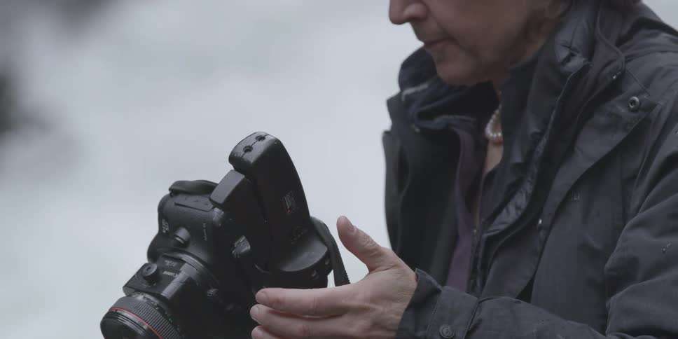 A person adjusts their camera near the water