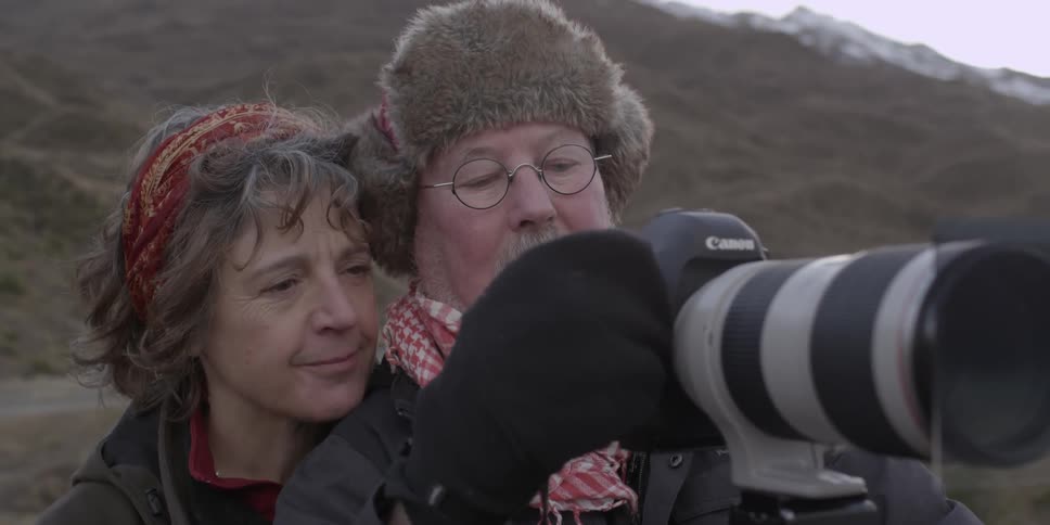 A man and woman look at a camera
