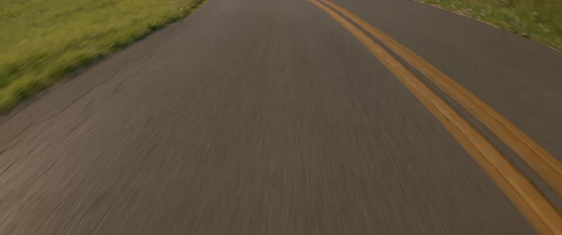 A vehicle travels on a cracked asphalt road with a double yellow line