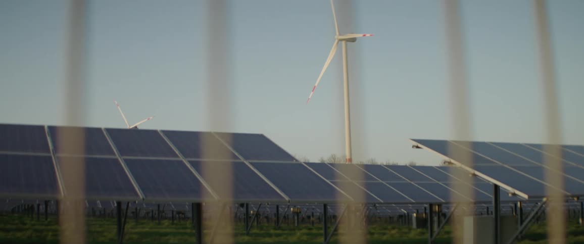 Wind turbine and solar panels behind a metal fence at sunrise