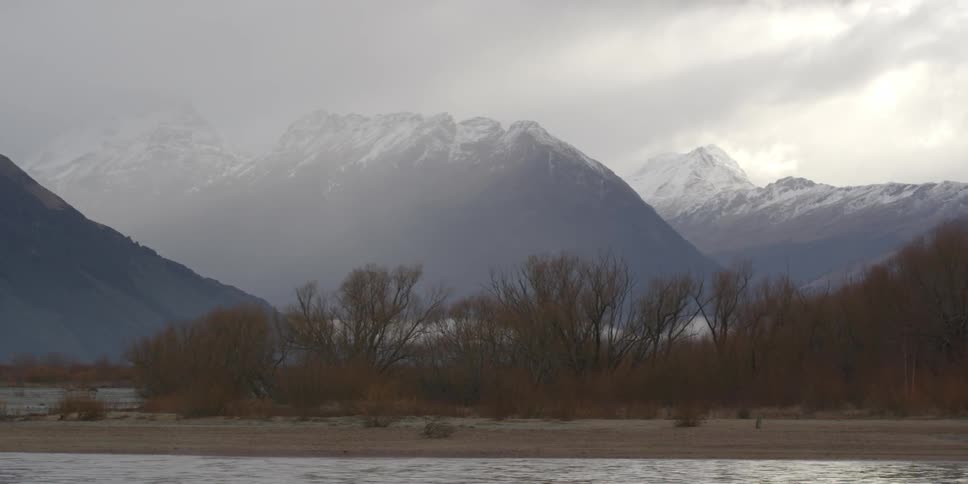 Mountains are in the distance past this shore with snow on top