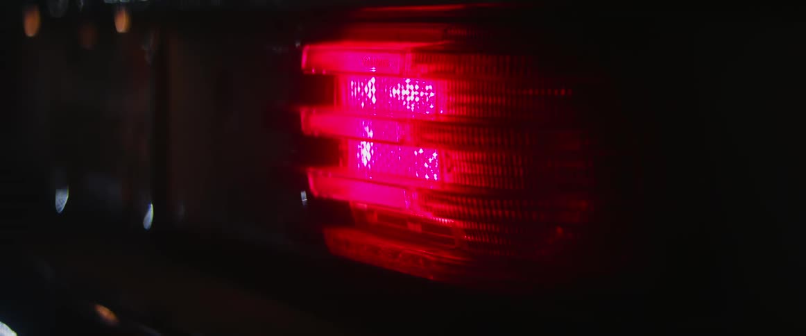 The tail light to a vehicle lit up red and flaring at night