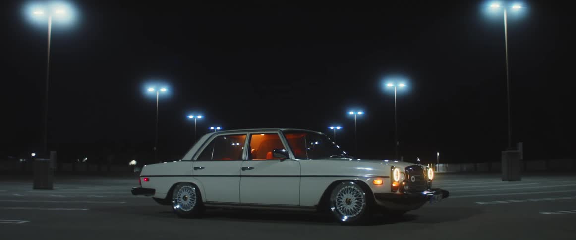 Older vehicle parked in vacant parking lot with headlights on at night