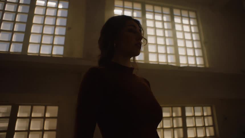 Woman performer standing in one spot with her eyes clothes in front of large windows letting the light in