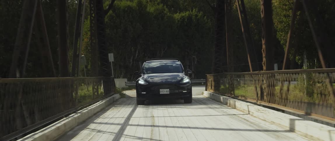 A black electric vehicle turns onto a bridge in the woods