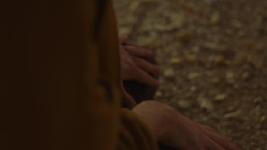 A close up of a person sitting on the ground putting their hands out while rain falls on them
