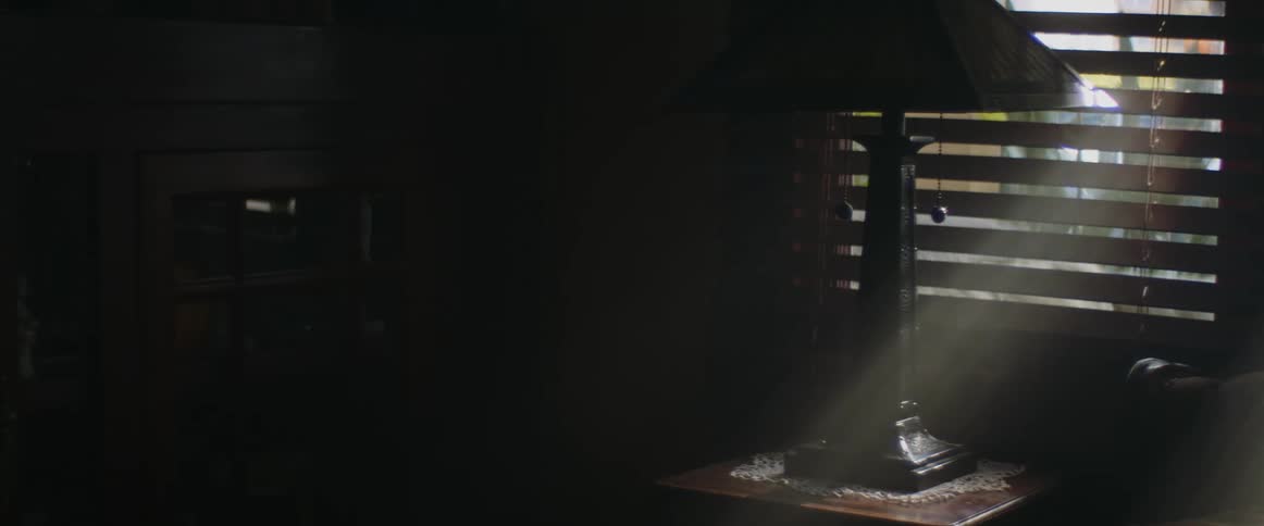 Sunlight rays shine through blinds on to table lamp