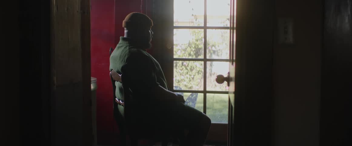 A man sitting in a chair through a door way in front of a window