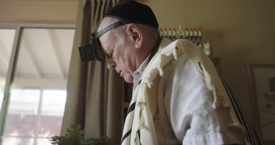 Old jewish man doing morning prayer ceremony during the day in house