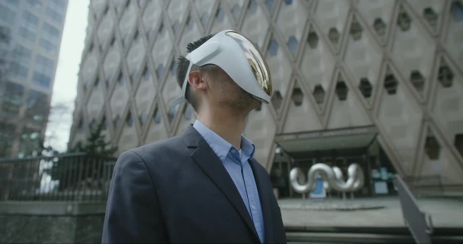 A man standing out front of a tall building while wearing a white full face head set with a gold plating on the front