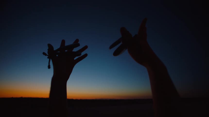 In a dark field with a dark cloud overhead in this surreal setting two hands are seen dancing within the cloud creating a mystical and captivating visual