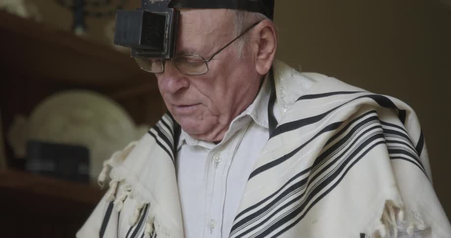 Older jewish man in vestments reciting morning prayers during the day